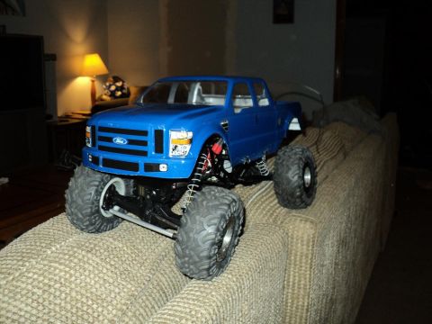 2008 Ford F-250 - This RC monster truck, resembling a 2008 Ford F-250, features oversized tires and a bright blue body, perched on a textured couch.