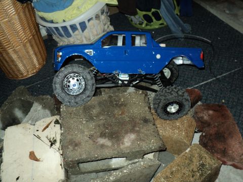 2008 Ford F-250 - A blue RC truck is shown on a rocky terrain, with household items in the background.