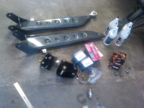 1986 Ford Bronco - Various automotive parts, including control arms and fluids, are laid out on a concrete surface.