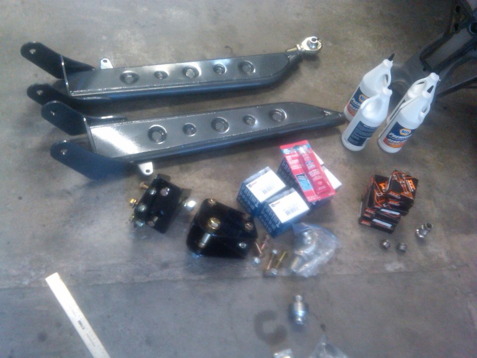 pair of control arms, boxes of parts, and bottles of fluid on concrete floor