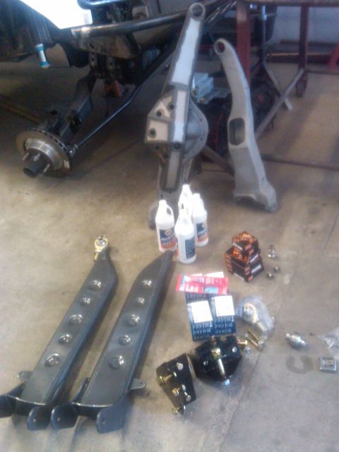 1986 Ford Bronco - Various suspension parts, including control arms and a differential housing, are laid out with bottles of fluid and hardware.