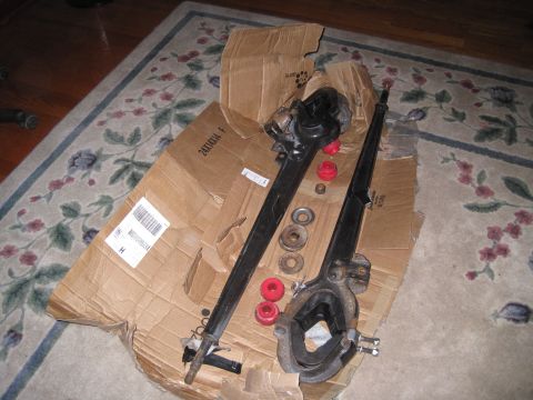 1979 Ford Bronco - Vehicle suspension parts, including control arms and red bushings, are laid out on a cardboard box on a rug.