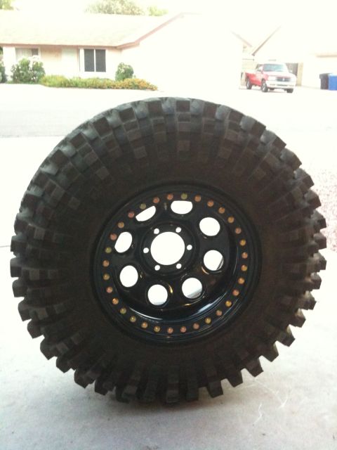 Suzuki Samurai - A close-up of a off-road tire mounted on a black wheel with decorative beadlock bolts.