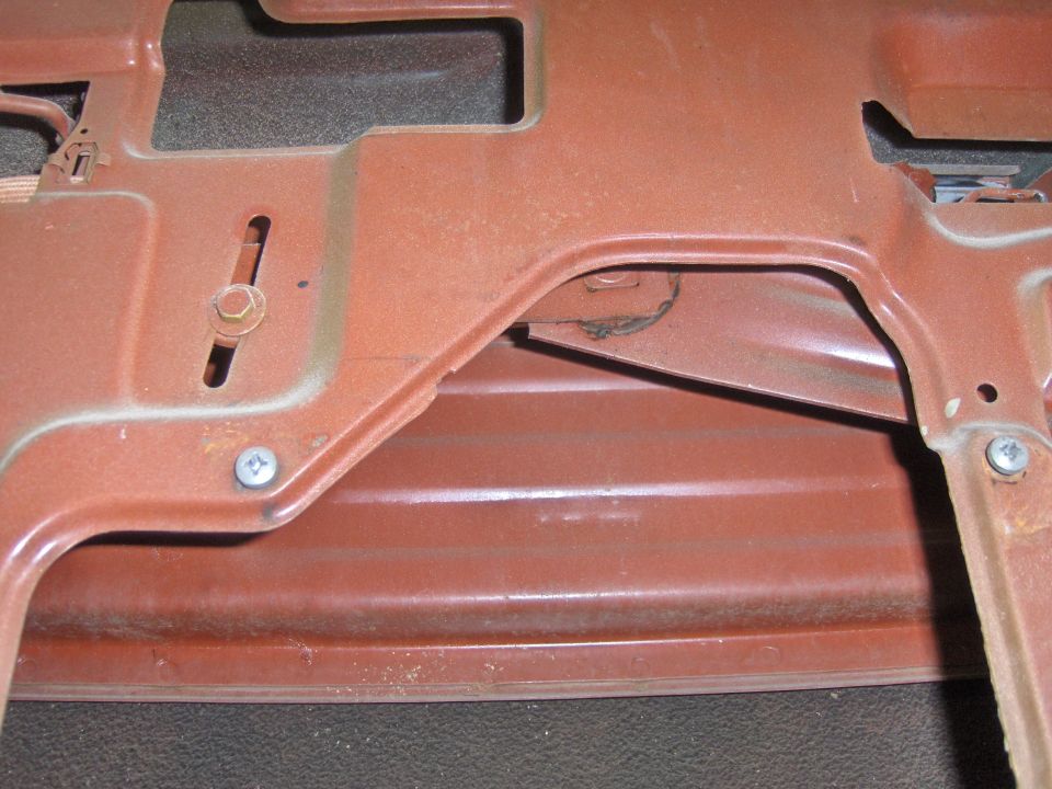 Close-up of a rusty brown metal bracket with visible screws and a slotted adjustment hole