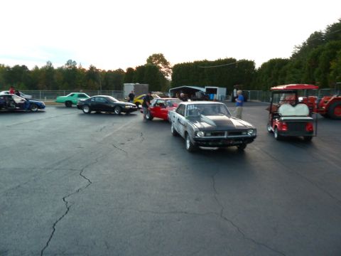 1992 Ford Mustang - Cars and a golf cart are gathered on a cracked asphalt surface, possibly at a race track, under an overcast sky.