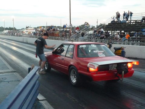 1992 Ford Mustang - A red 1992 Ford Mustang drag car is on the race track with spectators in the background.