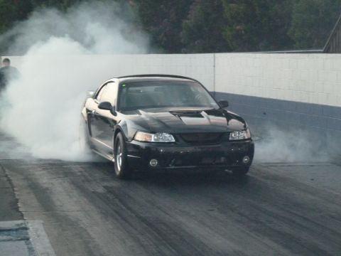 1992 Ford Mustang - A black coupe performs a burnout on a drag strip, creating a large cloud of smoke.