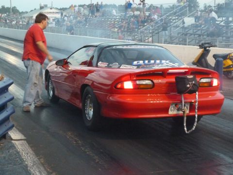 1992 Ford Mustang - Rear view of a red drag car on a race track, with a man standing next to it.
