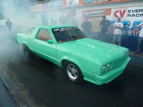 1992 Ford Mustang - A mint green coupe drag car is seen on the track, emitting smoke from its tires. The windshield displays a banner for "THE HOT ROD SHOP".