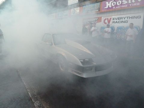 1992 Ford Mustang - A silver drag car performs a burnout, enveloped in smoke, at a racing event.