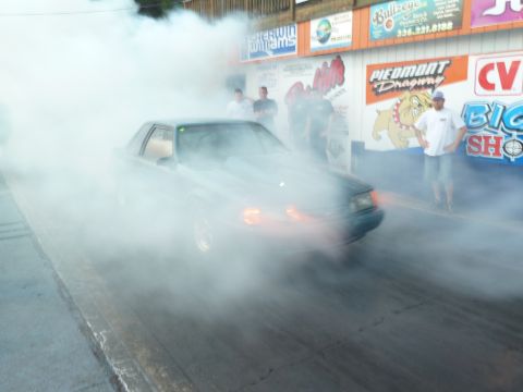 1992 Ford Mustang - A car performs a burnout on a drag strip, generating a large cloud of smoke.