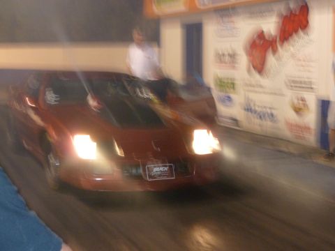 1992 Ford Mustang - A red sports car speeds down a track, illuminated by its headlights and the surrounding lights.