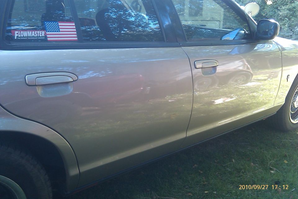 Side view of a tan sedan with an American flag and Flowmaster sticker on the rear window