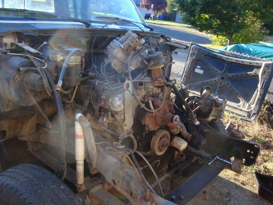 Stripped engine bay of a truck showing intake, distributor and loose wiring in a driveway