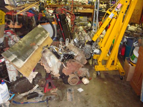 1989 Ford Bronco - Two pulled V8 engines sit on the floor of a cluttered garage, a rusty short block on a red engine stand cradle with its harmonic balancer,…