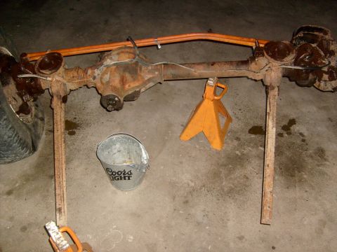 1994 Ford Bronco - A rusty rear axle assembly is supported by jack stands, with a bucket nearby.