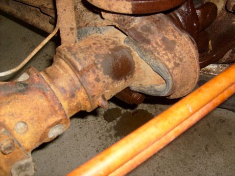 1994 Ford Bronco - Detail of a heavily rusted suspension part, possibly from a vehicle, with an orange pipe visible.