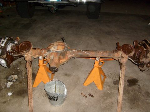 1994 Ford Bronco - Rear axle assembly removed from a vehicle and placed on jack stands for work. A bucket sits on the floor.