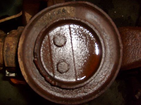 1994 Ford Bronco - A close-up view of a heavily rusted metal component, possibly from a vehicle's drivetrain, with two visible bolts and a small amount of oil.