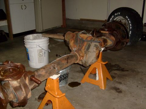 1994 Ford Bronco - Front axle assembly from a 1994 Ford Bronco, supported by orange jack stands in a garage.