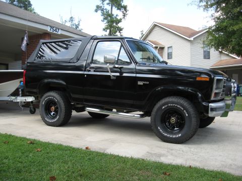 1986 Ford Bronco - A black Ford Bronco is parked in a driveway with a boat trailer attached.