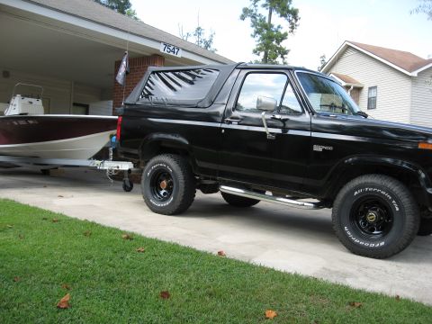 1986 Ford Bronco - Black Ford Bronco towing a boat trailer in front of a house.
