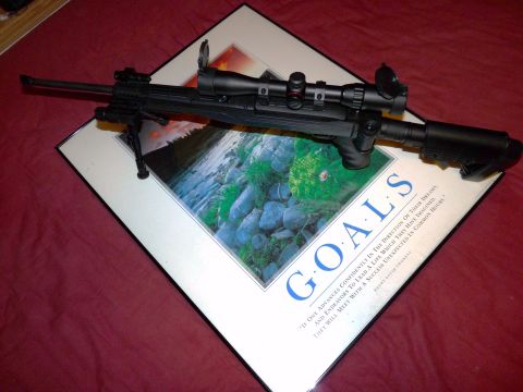 2006 Ford E350 - A rifle with a scope and bipod is placed on a framed print that says "GOALS".
