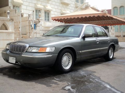 2001 Mercury Grand Marquis - A gray 2001 Mercury Grand Marquis sedan is parked in front of a building.