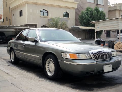 2001 Mercury Grand Marquis - A gray Mercury Grand Marquis is parked on a paved surface in front of a building with a covered carport.