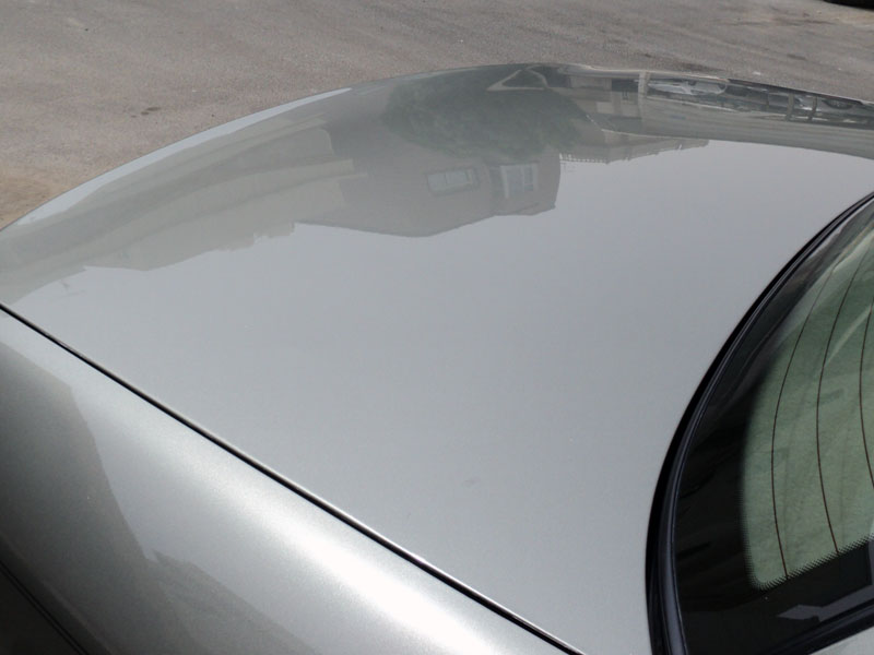 Silver car roof and hood with reflections of buildings and sky. A Supermotors.net watermark is visible