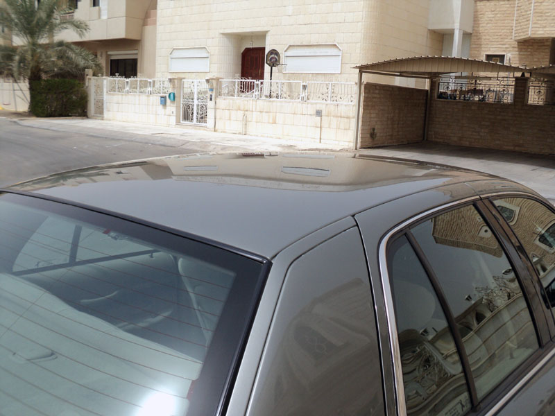 Gray sedan roof and rear window, showing reflections of buildings