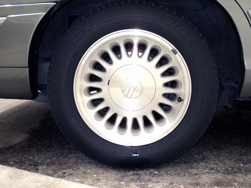 Close-up of Mercury alloy wheel with oval slots and Michelin tire on a silver sedan