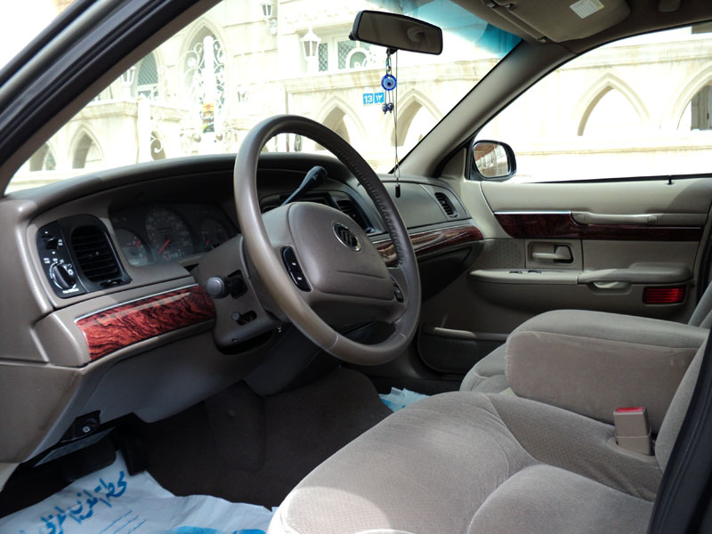 Tan interior of Mercury Grand Marquis with woodgrain trim, evil-eye charm on mirror, plastic-covered floor