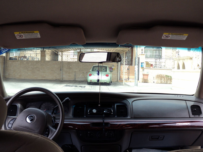 Interior view from a Mercury Grand Marquis looking out at a light green VW Beetle parked in a driveway