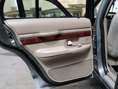 2001 Mercury Grand Marquis - Interior view of a car's rear passenger door, showing the tan door panel with wood grain trim and speaker grille.