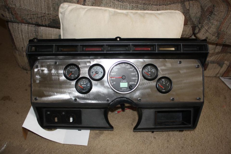 Dashboard instrument cluster with multiple gauges, including a speedometer, boost gauge, and oil pressure gauge. It has a brushed metal finish