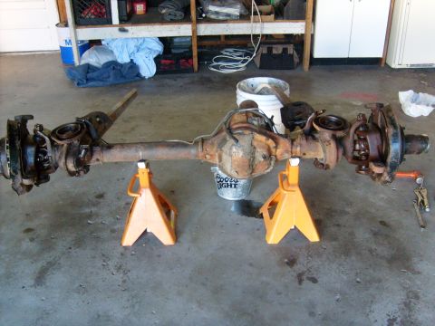 1994 Ford Bronco - Front axle assembly, likely from a 1994 Ford Bronco, is supported by jack stands in a garage setting.