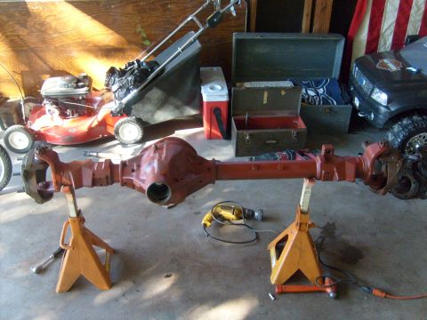 1994 Ford Bronco - A vehicle's rear axle assembly is displayed on jack stands in a garage, with a lawnmower and tools nearby.