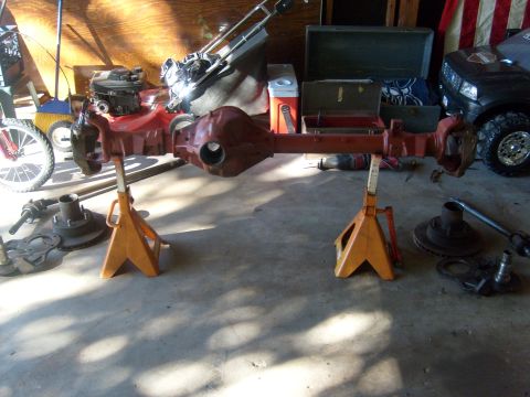 1994 Ford Bronco - Axle assembly displayed on jack stands, with a lawnmower and a black SUV visible in the garage.