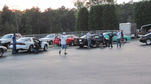1992 Ford Mustang - A group of people work on a white coupe with its door open, possibly a Pontiac Firebird, at an outdoor event.