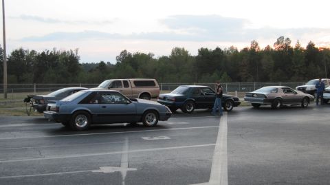 1992 Ford Mustang - Multiple cars and a truck line up on a drag strip under a cloudy sky.