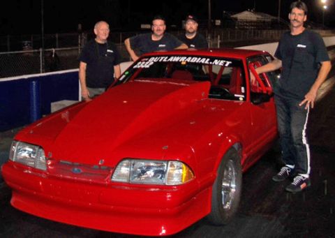 1992 Ford Mustang - A red 1992 Ford Mustang, modified for racing with a prominent hood scoop and roll cage, is displayed with its crew.