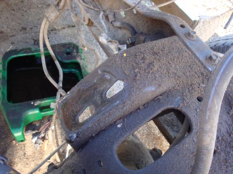 1989 Ford Bronco - Close-up of a dusty, dirt-caked front crossmember/engine mount bracket on a truck chassis, shot from above on a gravel driveway with wiring…