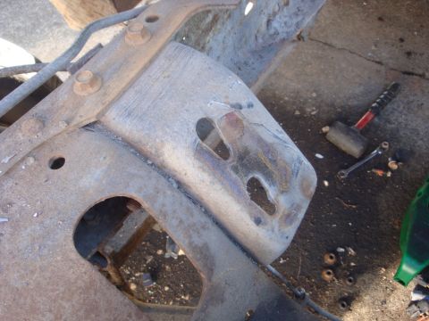 1989 Ford Bronco - Overhead close-up of a bare truck frame crossmember with a freshly welded and ground-in bracket, showing heat-blued weld beads and slotted…