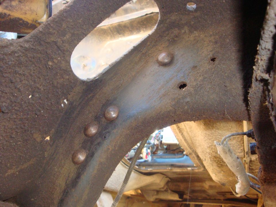 Rusty truck frame rail with a bracket ground off, showing bare steel and weld nubs