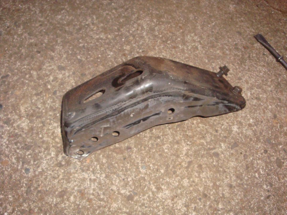 Greasy stamped-steel frame mount bracket removed and laid on concrete floor