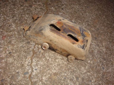 1989 Ford Bronco - A removed stamped-steel exhaust manifold heat shield lying on a concrete floor, heavily rusted and heat-discolored with brown and blue scal…