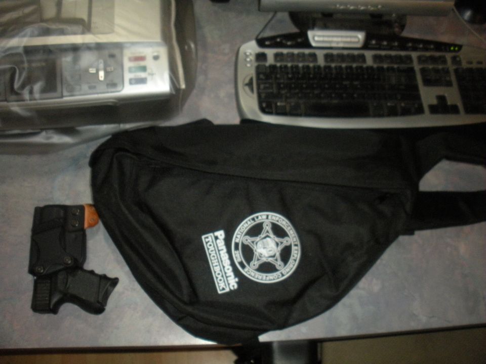 Black bag with "Panasonic TOUGHBOOK" and law enforcement logo, next to a handgun