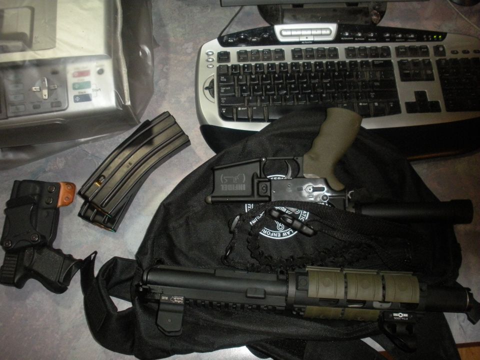 Firearms and magazines on a black bag next to a computer keyboard and a scanner