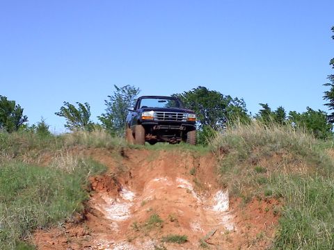 1994 Ford Bronco - A black Ford truck is positioned on a steep dirt incline under a clear blue sky.